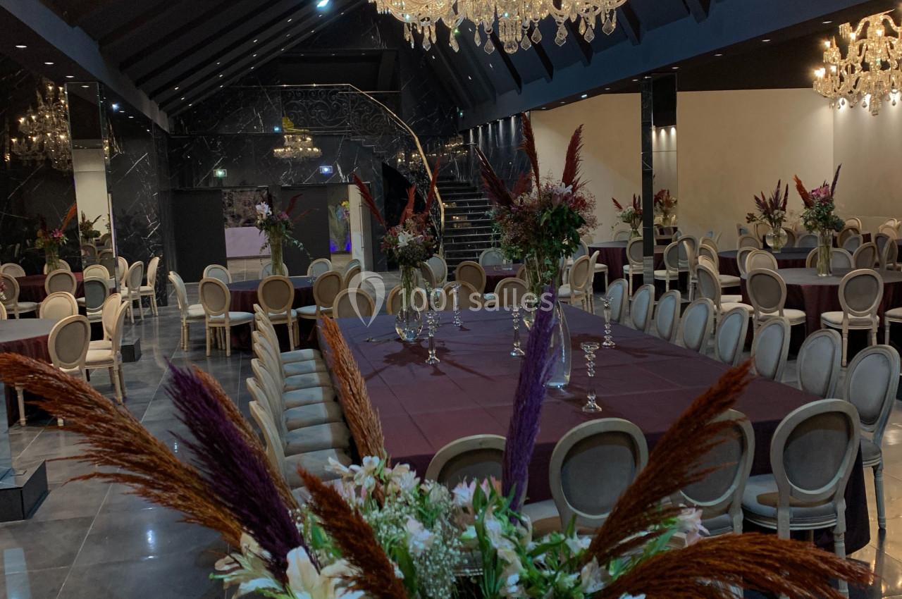 Salle de réception élégante avec tables rondes décorées de fleurs et lustres en cristal suspendus au plafond sombre.