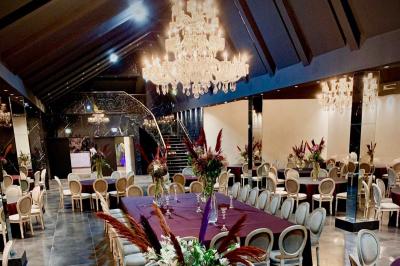 Salle de réception élégante avec tables rondes noires, chaises transparentes, lustres en cristal et décorations végétales.