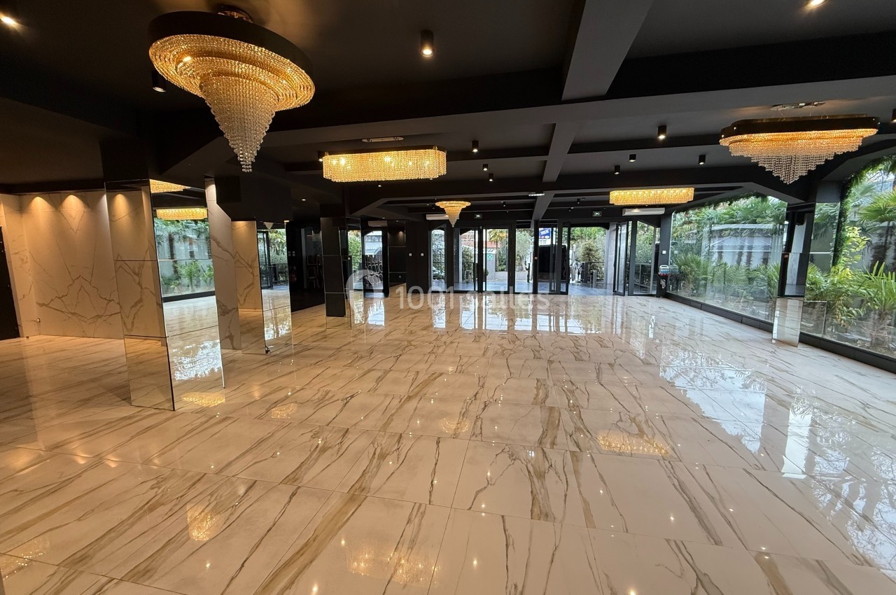 Salle spacieuse avec sol en marbre, lustres en cristal et grandes baies vitrées donnant sur un jardin.