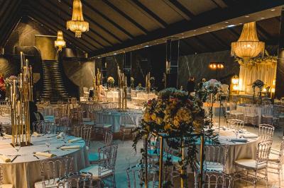 Salle de réception élégante avec tables rondes noires, chaises transparentes, lustres en cristal et décorations végétales.