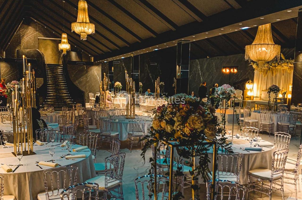 Salle de réception élégante avec tables dressées, chandeliers dorés, fleurs et lustres imposants.