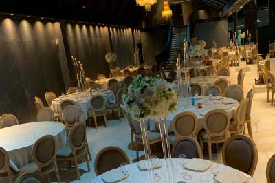 Salle de réception élégante avec tables rondes noires, chaises transparentes, lustres en cristal et décorations végétales.