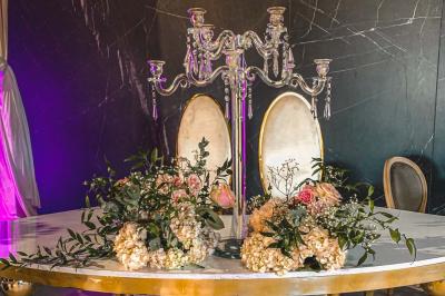 Salle de réception élégante avec tables rondes noires, chaises transparentes, lustres en cristal et décorations végétales.
