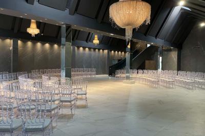 Salle de réception élégante avec tables rondes noires, chaises transparentes, lustres en cristal et décorations végétales.
