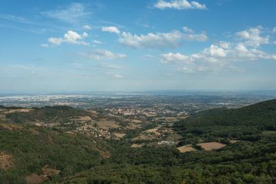 Vue aérienne d'une vallée verdoyante avec des collines, des villages et un ciel partiellement nuageux à l'horizon.