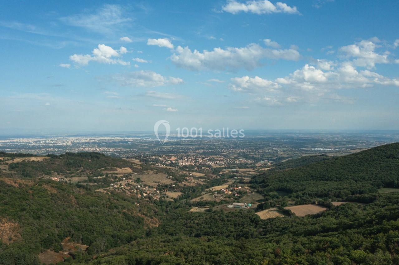 Vue aérienne d'une vallée verdoyante avec des collines, des villages et un ciel partiellement nuageux à l'horizon.