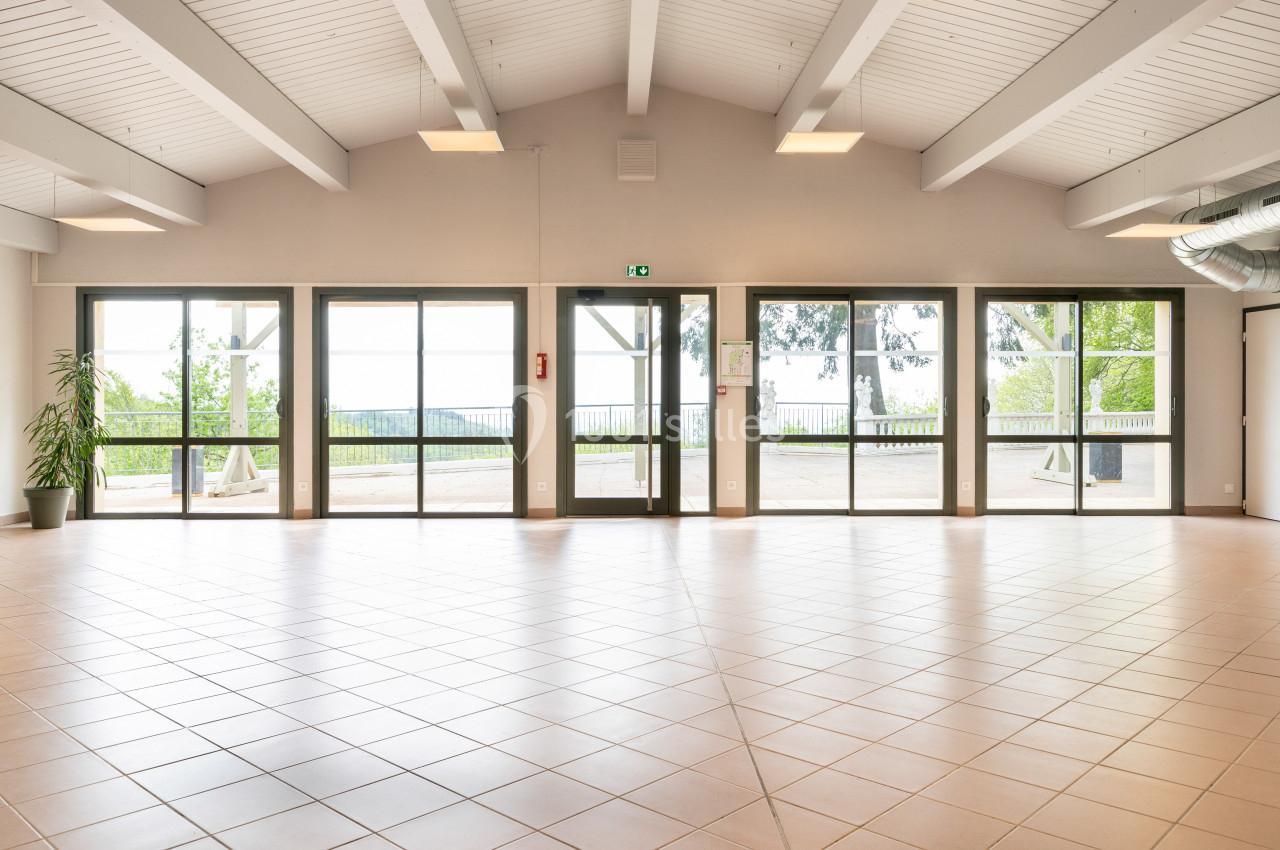 Salle lumineuse avec plafond en poutres blanches, grandes baies vitrées donnant sur un espace extérieur arboré.