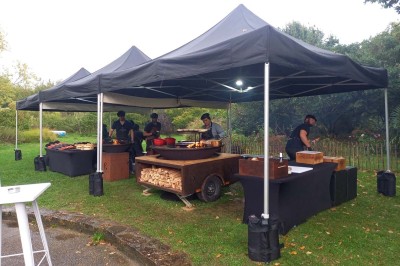 Miniature Location salle Névez (Finistère) - Jardins et Serres de Rospico #3 Grande salle lumineuse avec sol rouge, toit en verre, chaises blanches, comptoir et décorations suspendues.