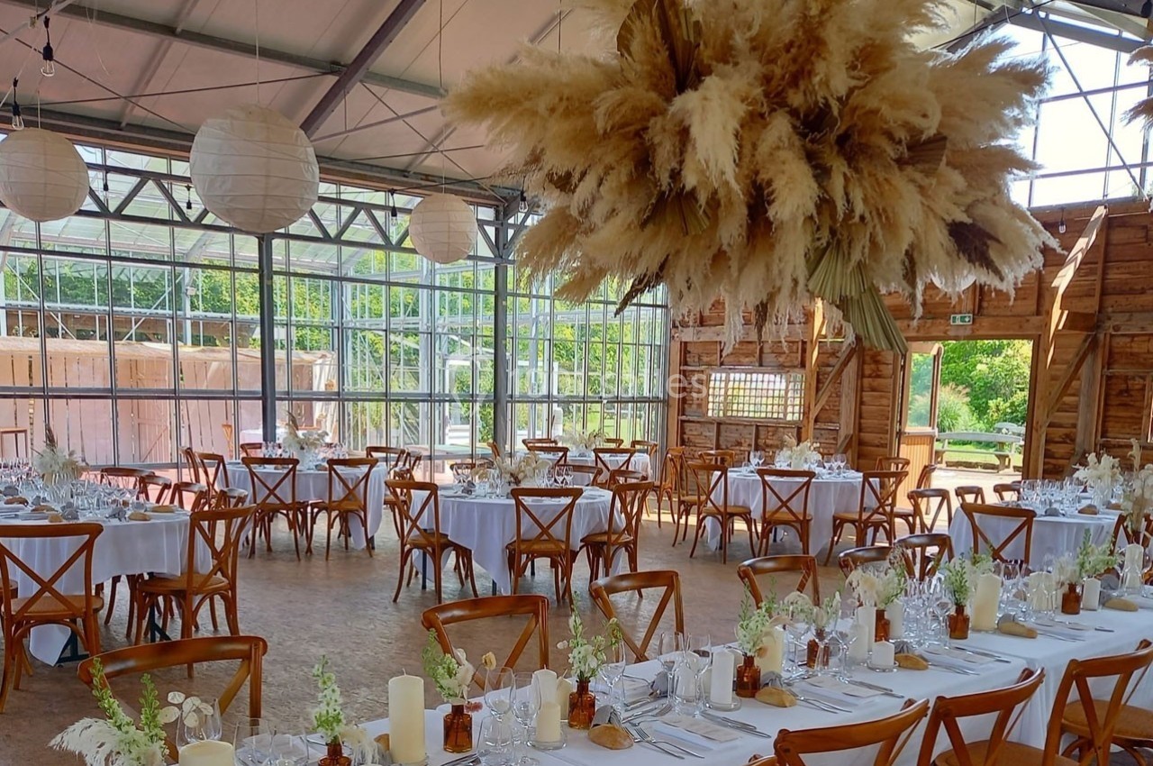Salle de réception lumineuse avec tables décorées de fleurs blanches et pampas suspendues au plafond.