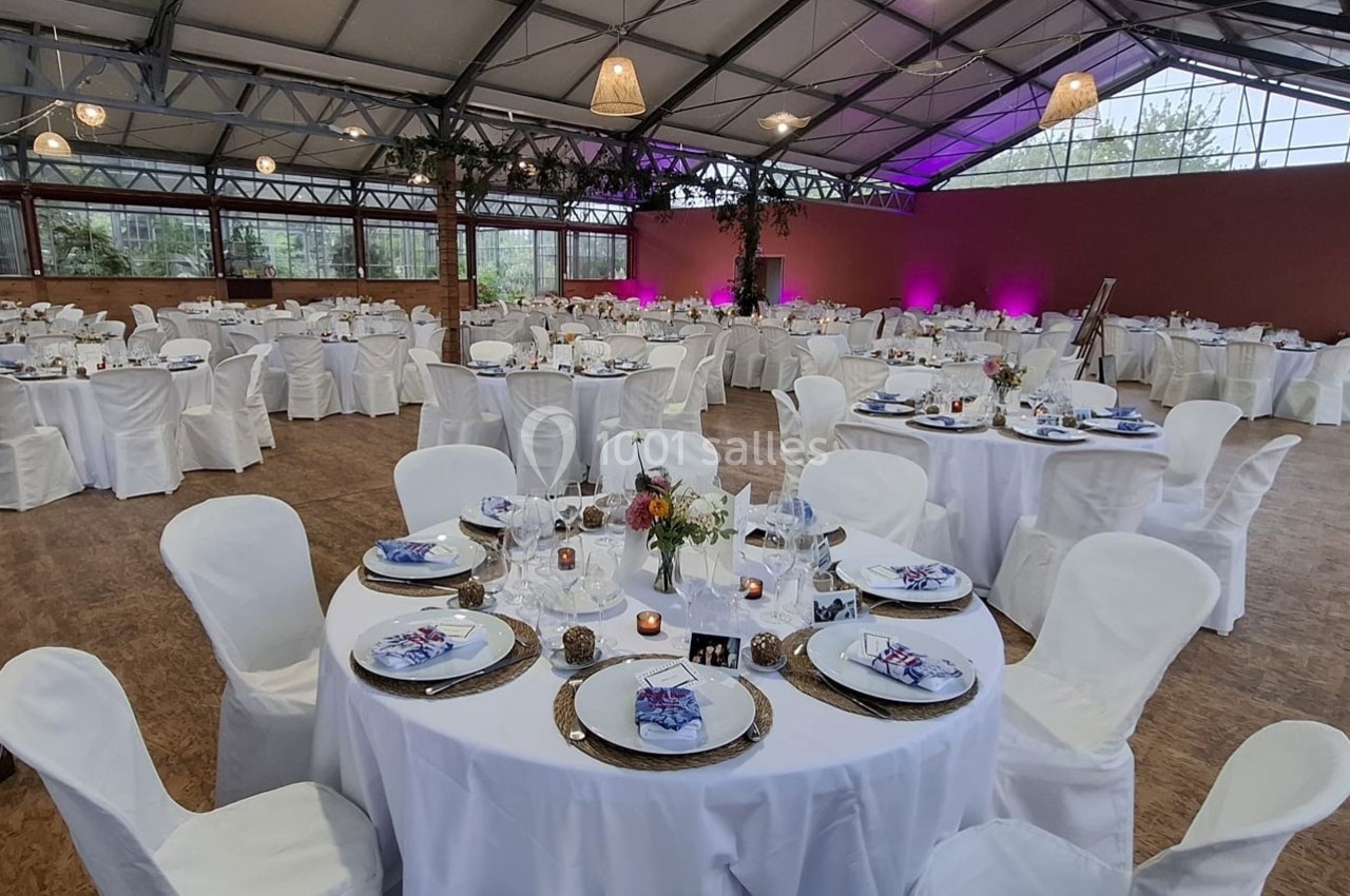 Salle de réception décorée avec des tables rondes dressées, nappes blanches et éclairage tamisé.