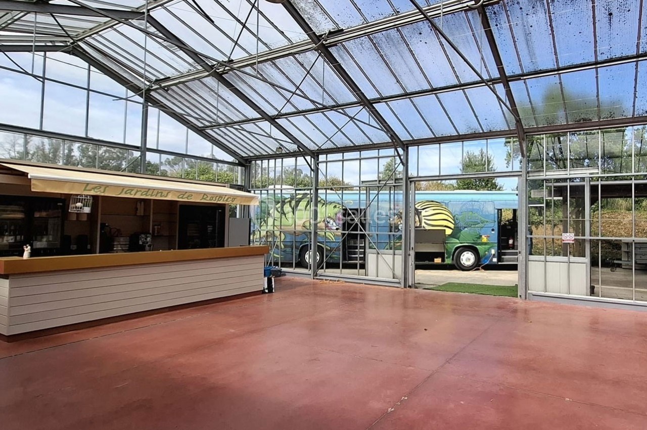 Intérieur d'une serre avec un comptoir en bois à gauche et un camion coloré visible à l'extérieur.