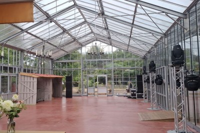 Miniature Location salle Névez (Finistère) - Jardins et Serres de Rospico #14 Grande salle lumineuse avec sol rouge, toit en verre, chaises blanches, comptoir et décorations suspendues.