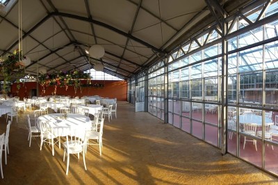 Miniature Location salle Névez (Finistère) - Jardins et Serres de Rospico #15 Grande salle lumineuse avec sol rouge, toit en verre, chaises blanches, comptoir et décorations suspendues.