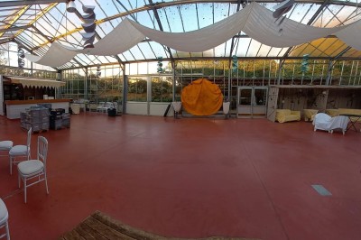 Miniature Location salle Névez (Finistère) - Jardins et Serres de Rospico #16 Grande salle lumineuse avec sol rouge, toit en verre, chaises blanches, comptoir et décorations suspendues.