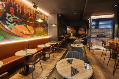 Salle de restaurant moderne avec murs en briques, tables en bois, chaises en cuir et éclairage tamisé.