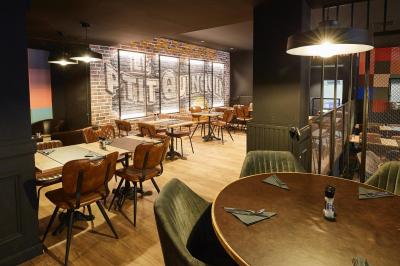 Salle de restaurant moderne avec murs en briques, tables en bois, chaises en cuir et éclairage tamisé.