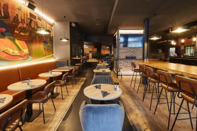 Salle de restaurant moderne avec murs en briques, tables en bois, chaises en cuir et éclairage tamisé.