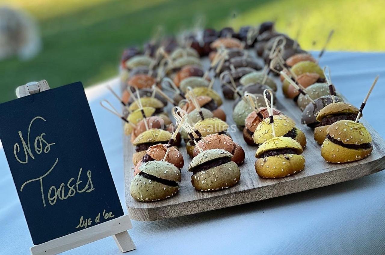 Plateau de mini-burgers colorés présentés sur une table, avec un tableau noir indiquant ’Nos toasts’.