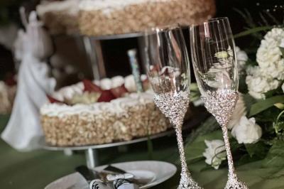 Deux flûtes décorées en cristal posées devant un gâteau à la crème et des fleurs blanches sur une table.