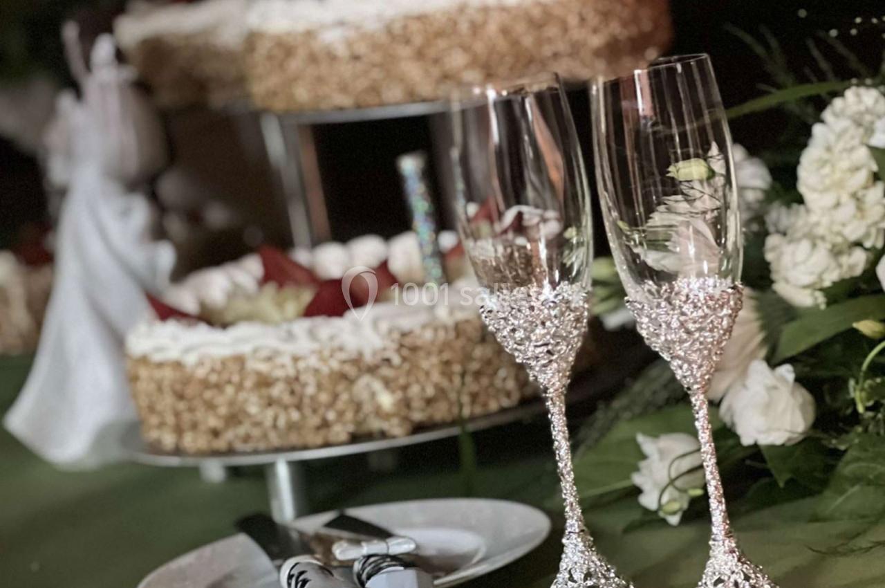 Deux flûtes décorées en cristal posées devant un gâteau à la crème et des fleurs blanches sur une table.