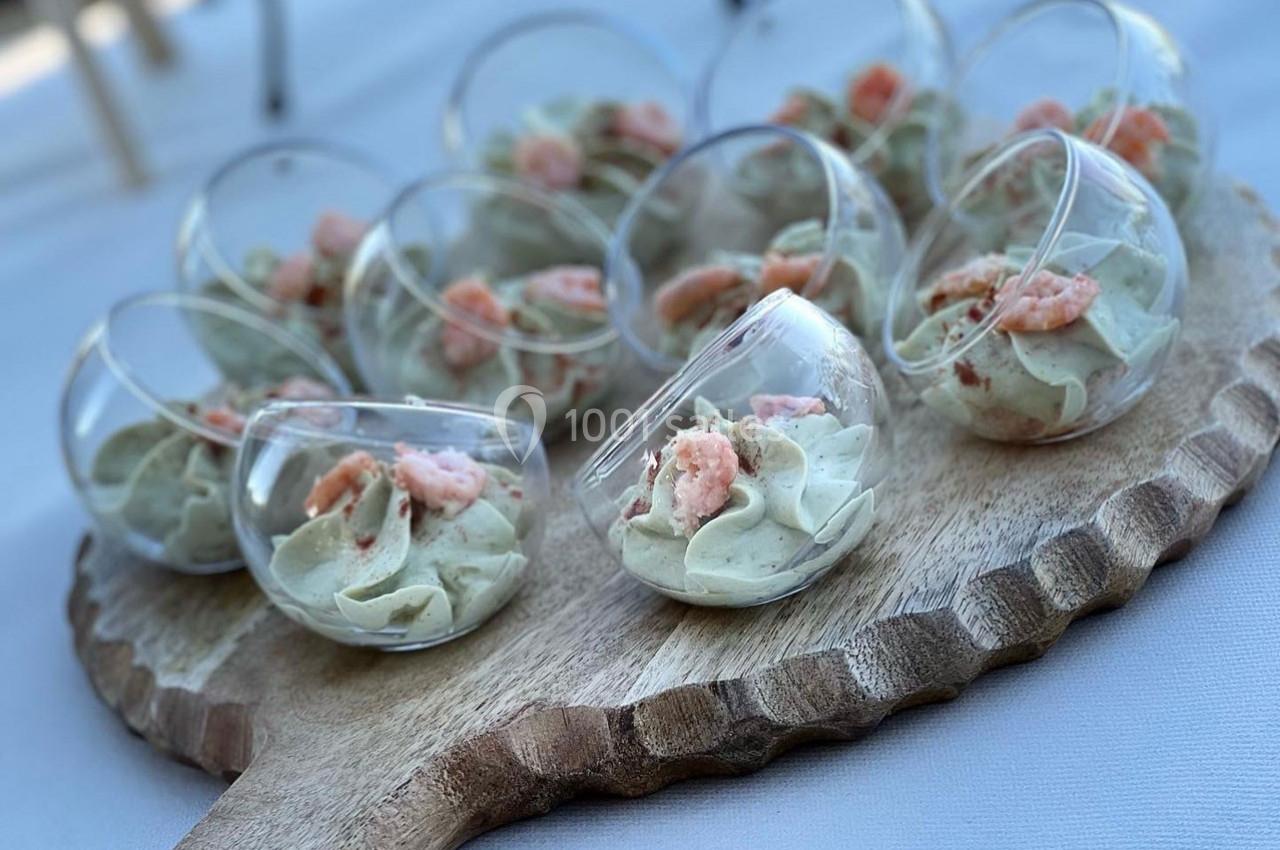 Verrines rondes contenant une mousse verte garnie de crevettes, présentées sur un plateau en bois.