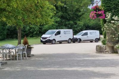 Portail en bois décoré de plantes grimpantes, donnant sur une cour ensoleillée bordée d'arbres et de végétation.