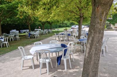 Portail en bois décoré de plantes grimpantes, donnant sur une cour ensoleillée bordée d'arbres et de végétation.