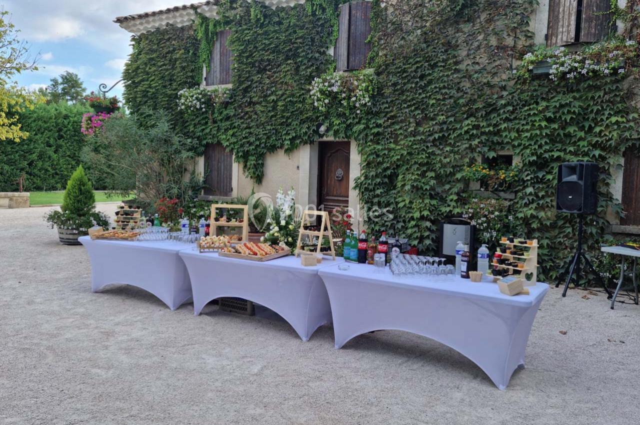 Table de buffet dressée en extérieur devant une maison en pierre couverte de végétation.
