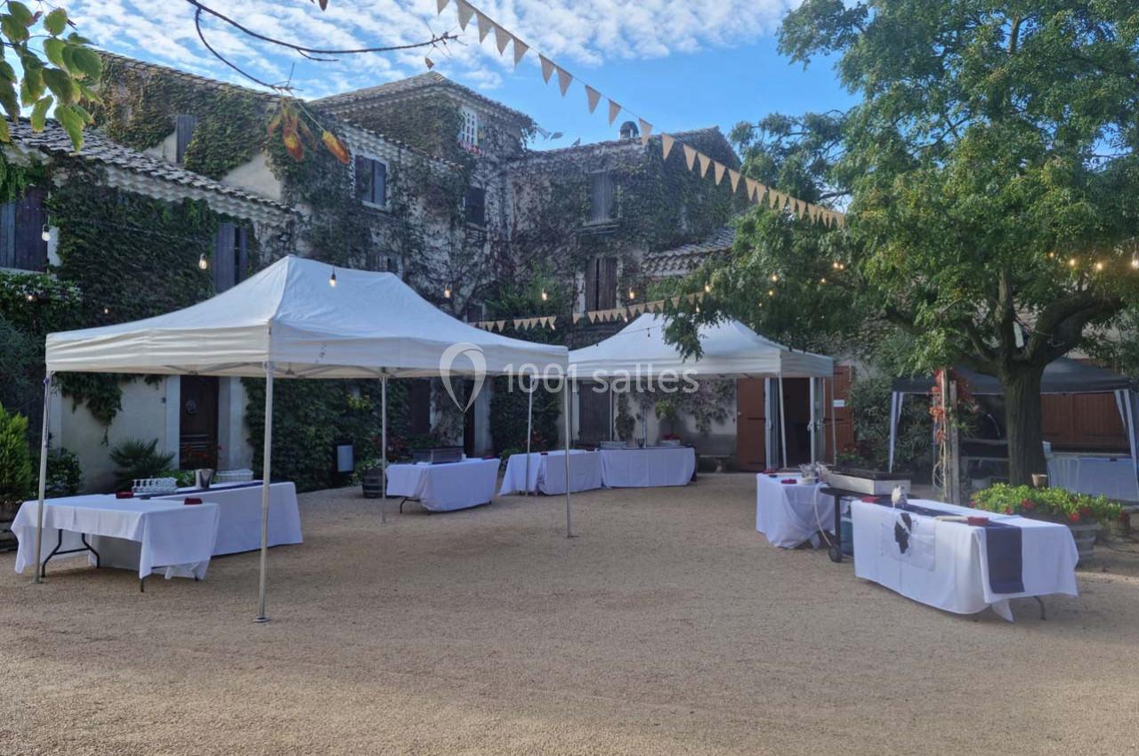 Cour extérieure avec des tentes blanches, tables dressées et décorations festives sous un ciel partiellement nuageux.