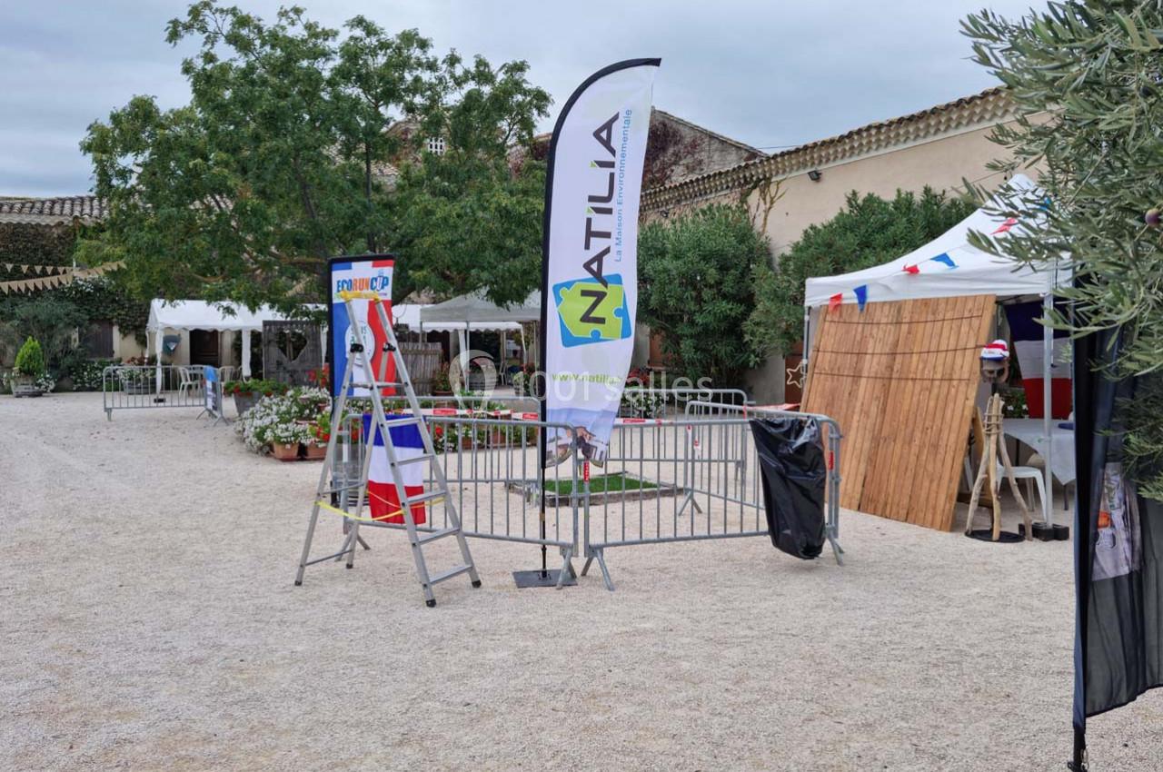 Cour extérieure avec des stands, une banderole ’NATILIA’, des drapeaux et des équipements d'installation.