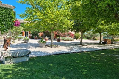 Bâtisse en pierre recouverte de lierre, entourée d'une cour gravillonnée et d'une pelouse sous un ciel bleu.