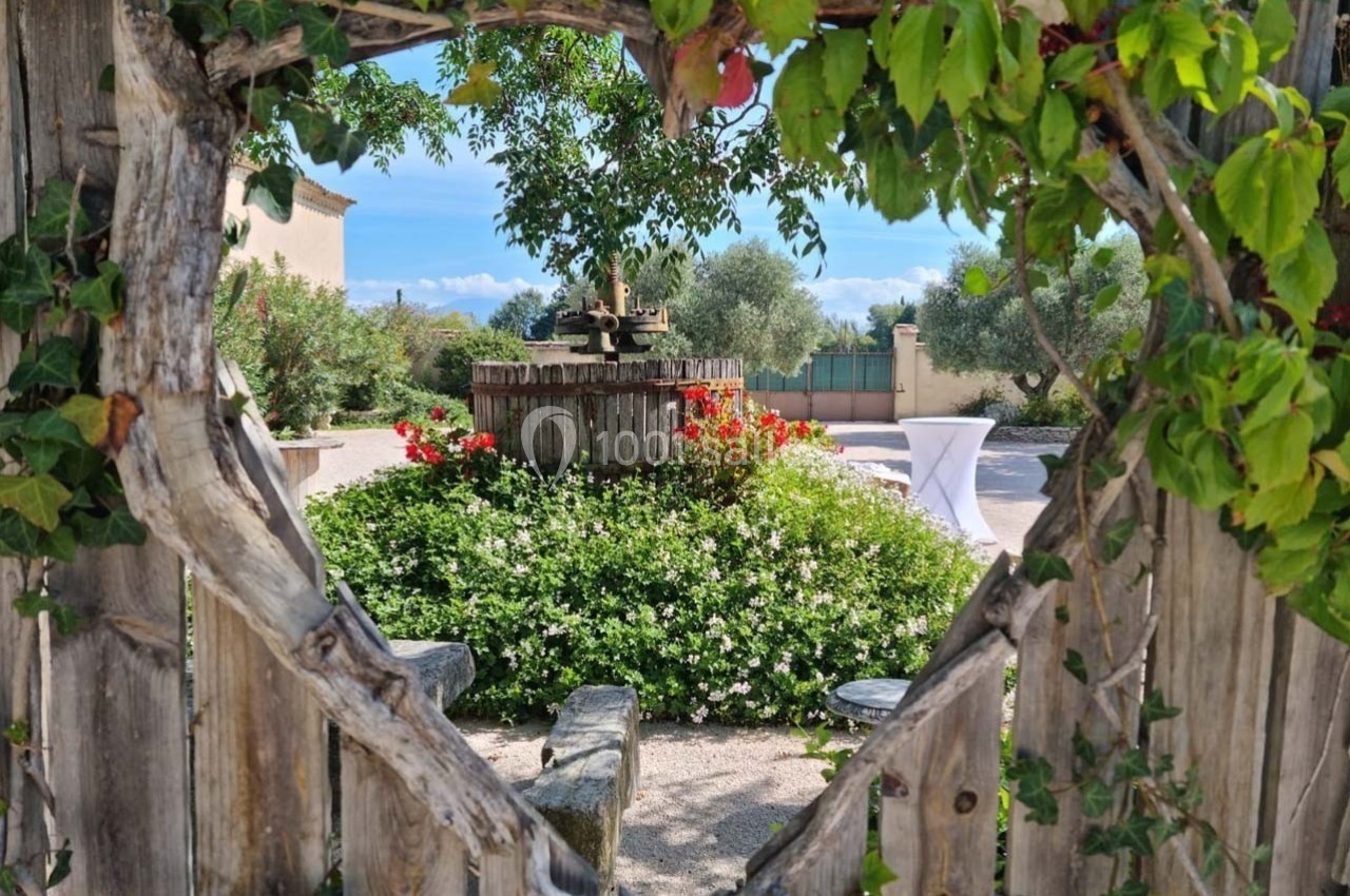Vue d'un jardin fleuri avec une vieille barrique en bois au centre, encadrée par une clôture en bois ornée de feuillage.