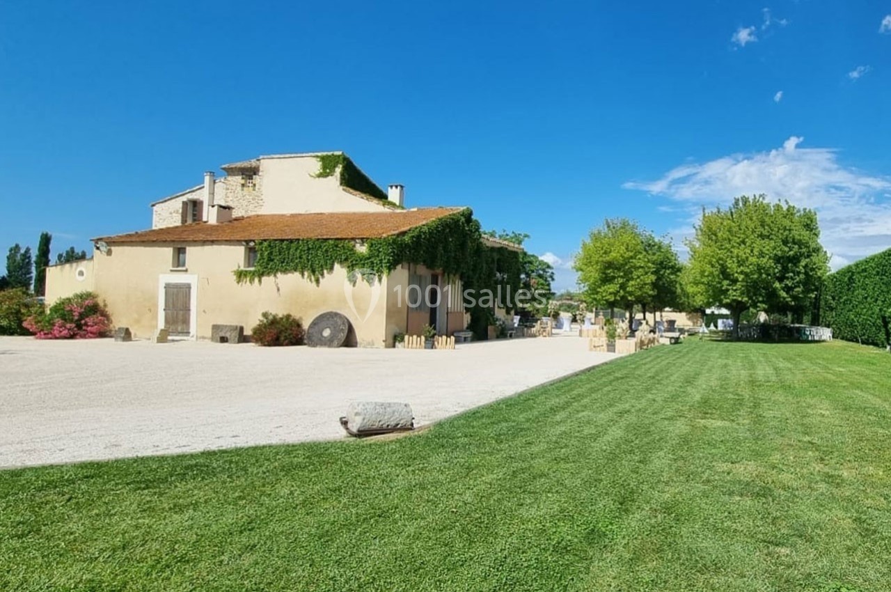 Bâtisse en pierre recouverte de lierre, entourée d'une cour gravillonnée et d'une pelouse sous un ciel bleu.
