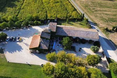 Bâtisse en pierre recouverte de lierre, entourée d'une cour gravillonnée et d'une pelouse sous un ciel bleu.