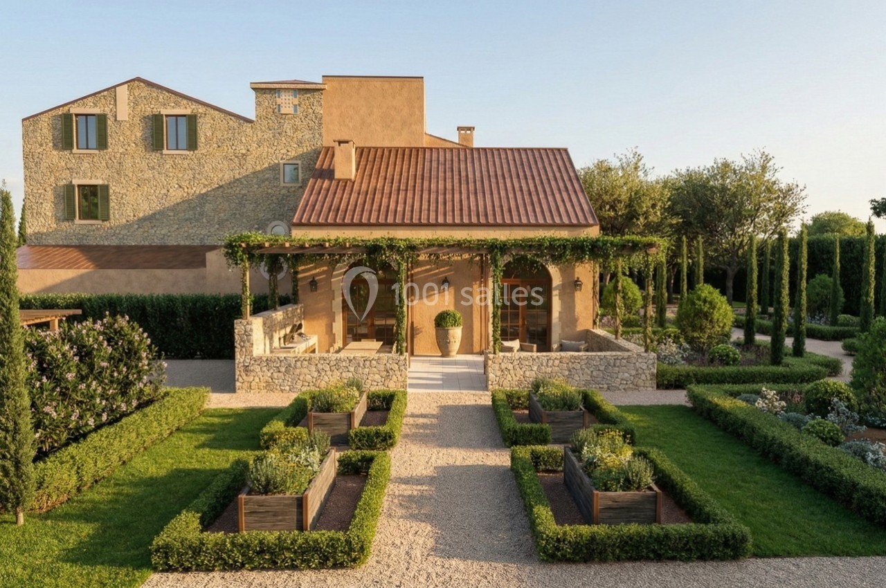 Façade d'une maison en pierre avec terrasse couverte, entourée d'un jardin aménagé et de chemins gravillonnés.