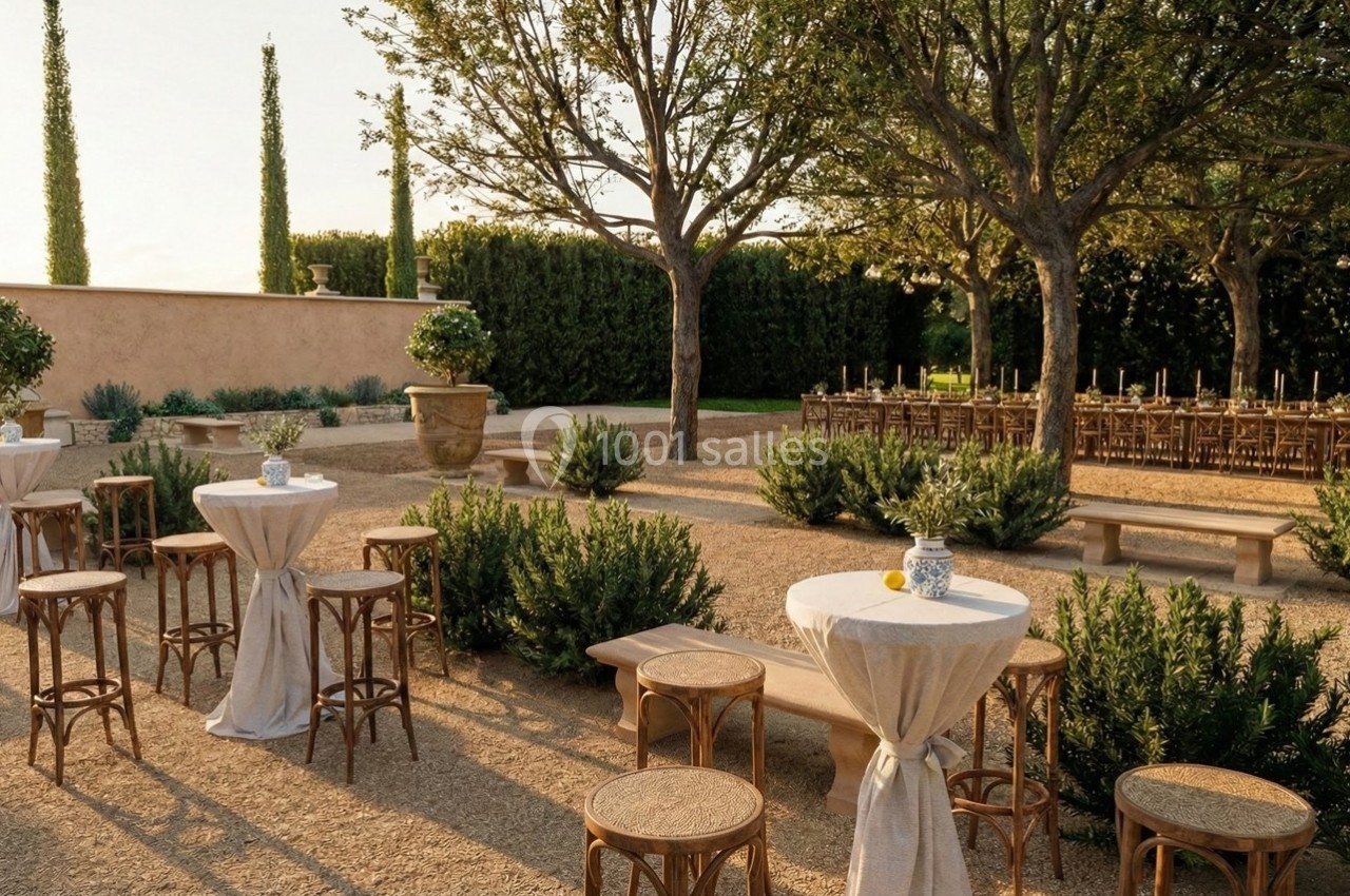 Terrasse extérieure aménagée avec tables hautes, chaises en bois et rangée de tables dressées sous des arbres.