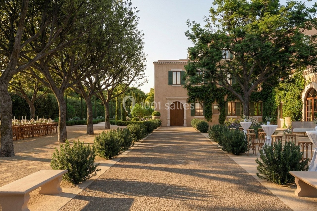 Allée bordée d'arbres menant à une maison en pierre, avec des tables dressées en extérieur sur les côtés.