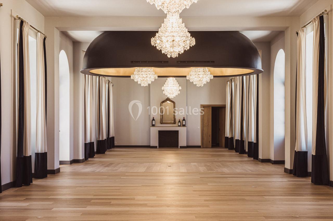 Salle spacieuse avec parquet clair, lustres en cristal, rideaux blancs et noirs, et cheminée encadrée de miroirs.