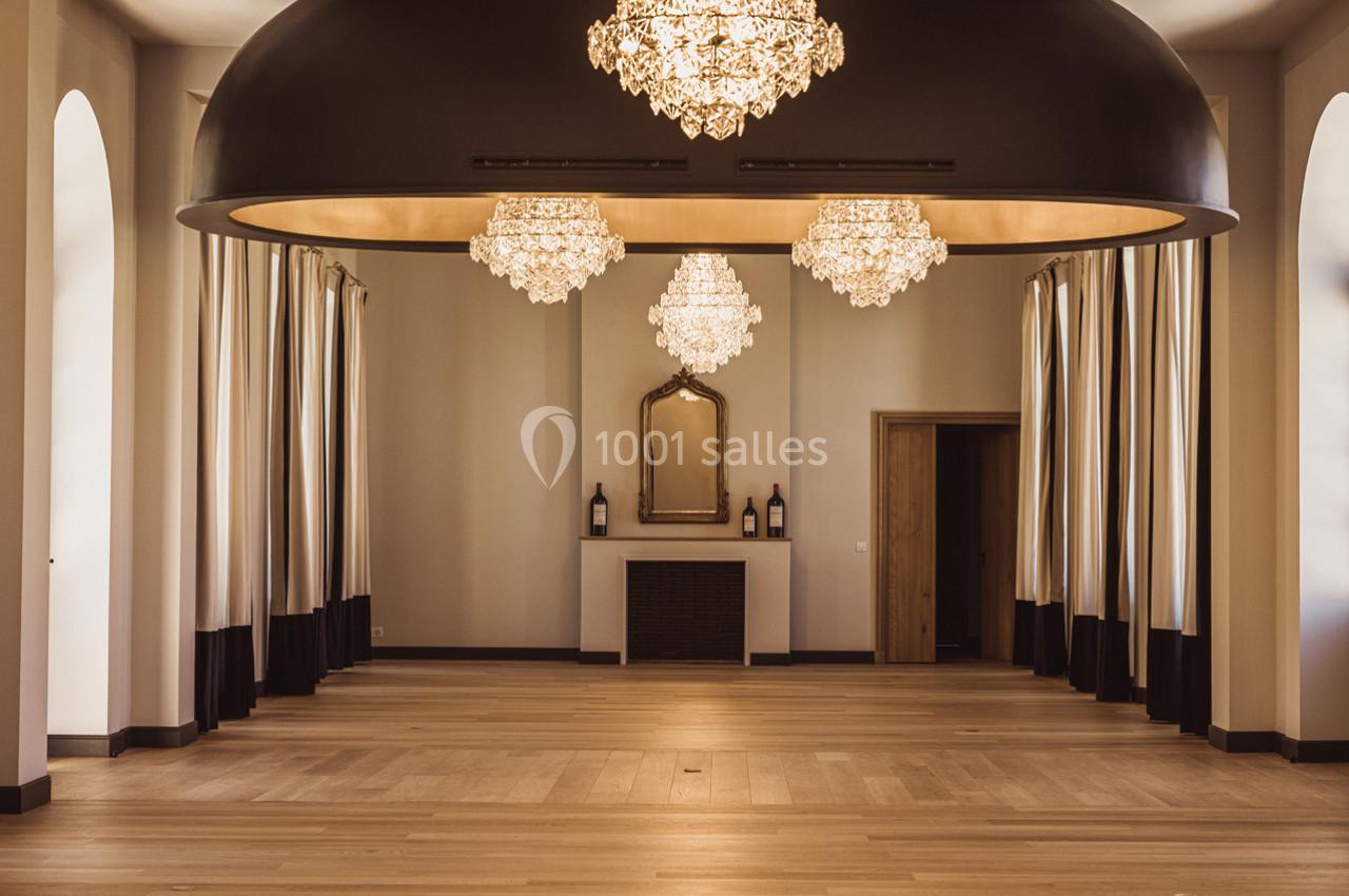 Salle élégante avec parquet en bois, lustres en cristal suspendus, rideaux encadrant des fenêtres et cheminée décorative.