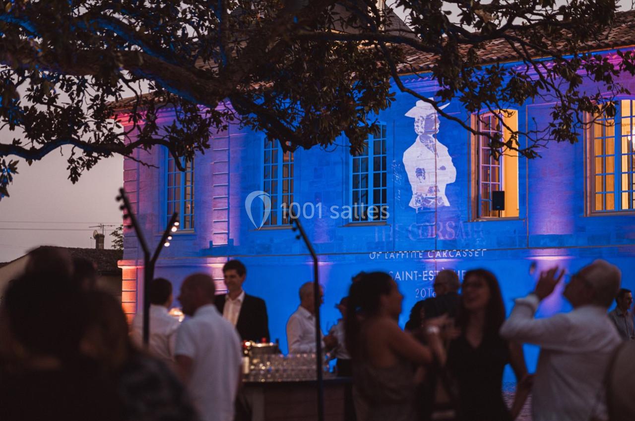 Des personnes discutent et profitent d'une soirée en plein air devant un bâtiment éclairé de lumières colorées.