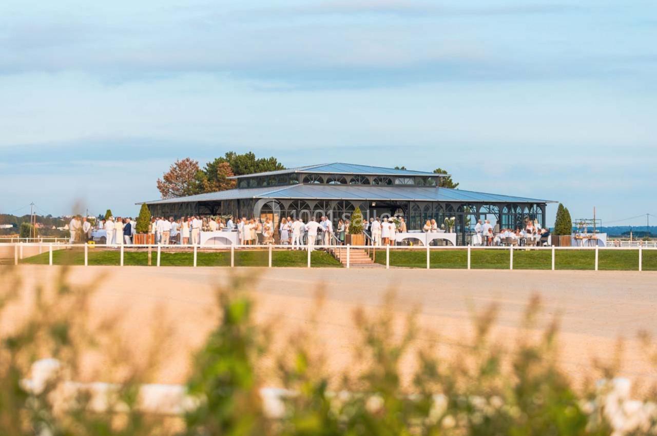 Vue d'un pavillon élégant entouré de convives en tenue blanche lors d'un événement en extérieur par temps clair.