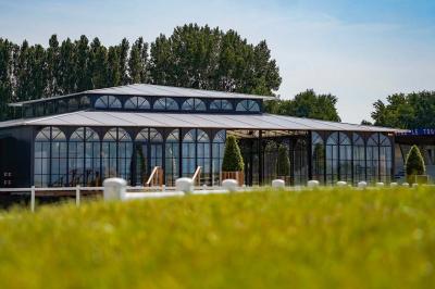 Bâtiment moderne avec une structure en verre et métal entouré de verdure, sous un ciel dégagé.