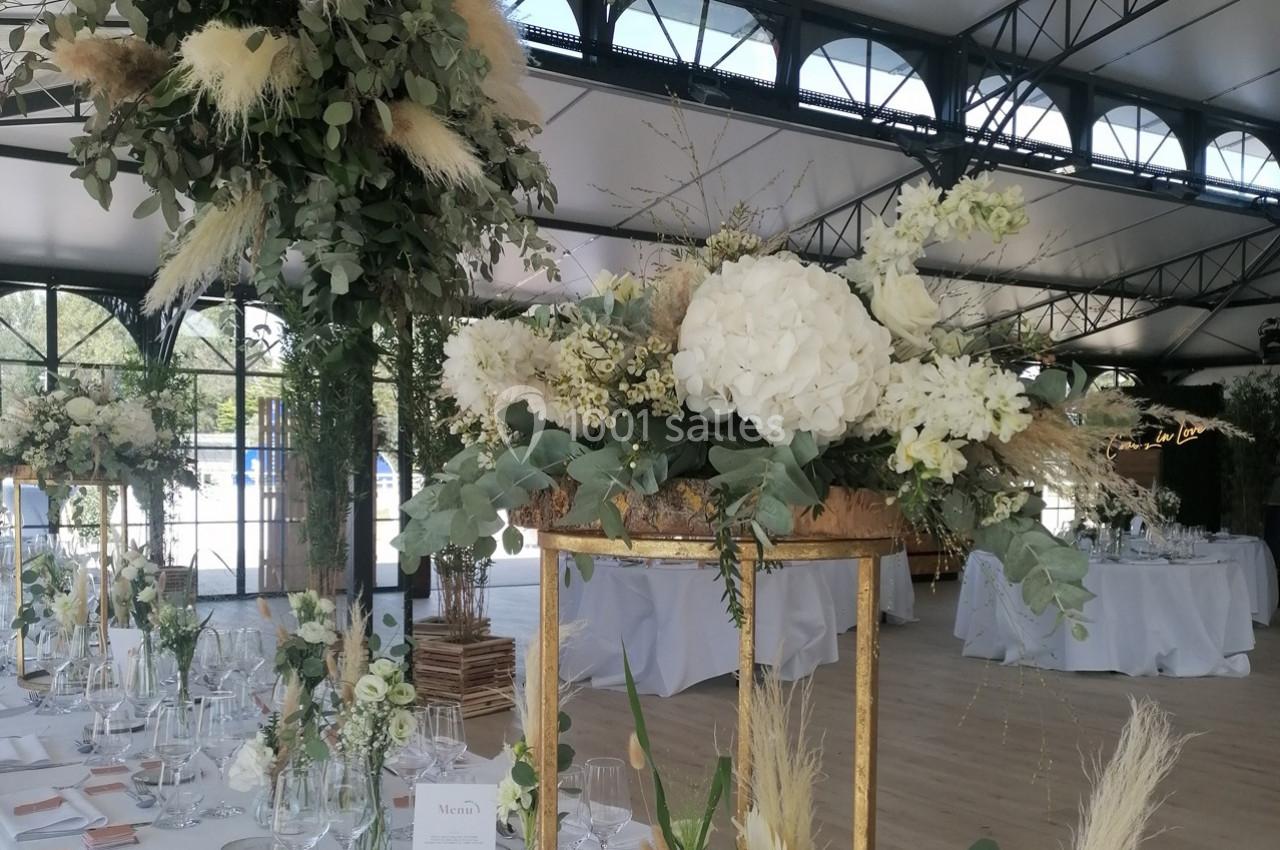 Décoration florale élégante avec hortensias blancs, feuillages et pampas, sur des tables dressées dans une salle lumineuse.