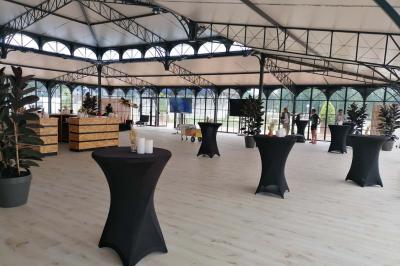 Bâtiment vitré éclairé en soirée, entouré d'arbres et d'une clôture blanche, avec quelques personnes à l'extérieur.