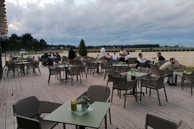 Bâtiment vitré éclairé en soirée, entouré d'arbres et d'une clôture blanche, avec quelques personnes à l'extérieur.