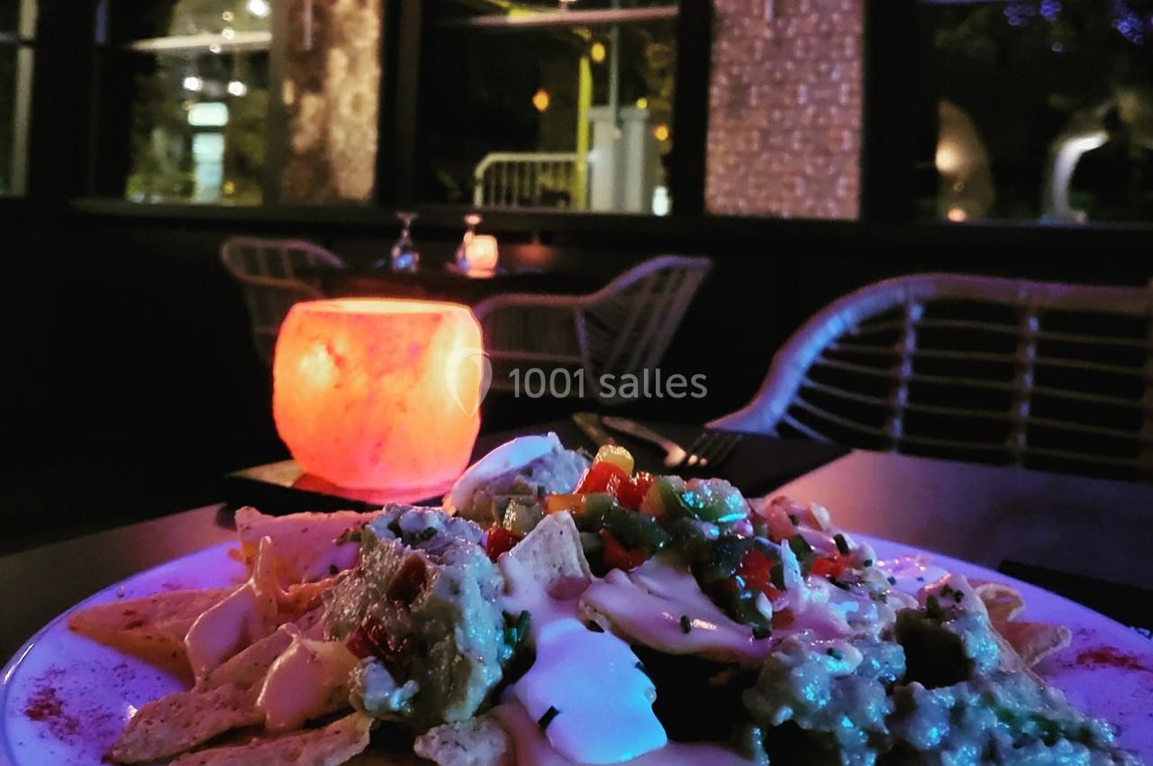 Assiette de nachos garnis de fromage, crème et légumes, posée sur une table dans un restaurant à l'éclairage tamisé.