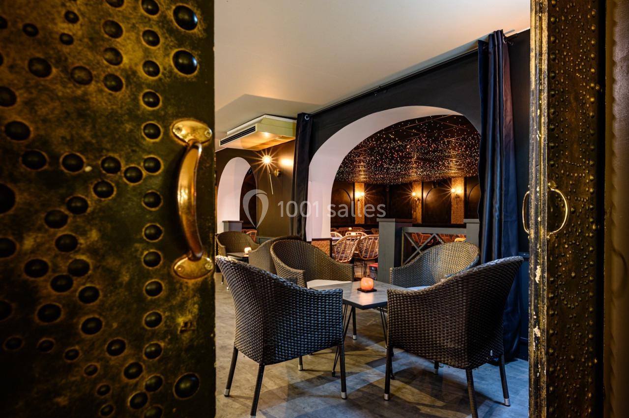 Salle avec des fauteuils en rotin, éclairage tamisé, murs sombres et plafond décoré de motifs étoilés.