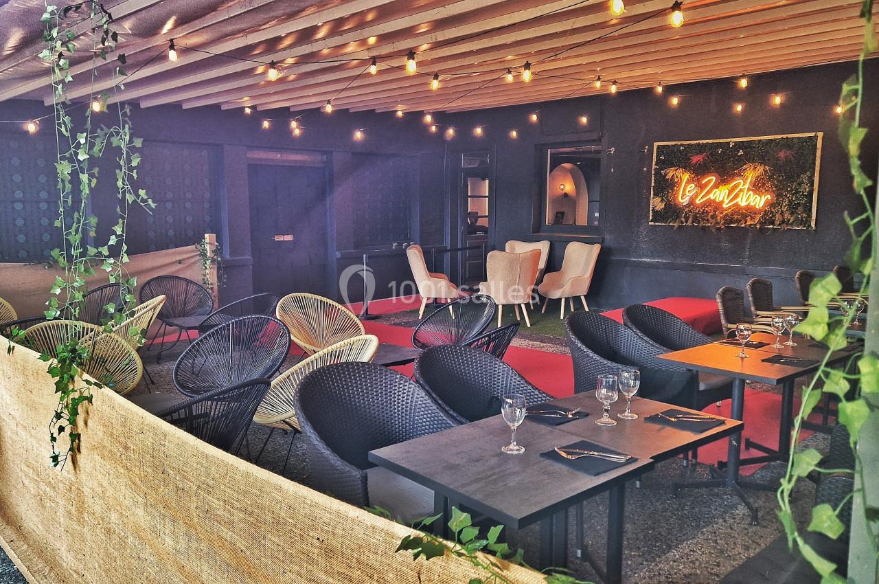 Terrasse couverte avec tables, chaises en rotin, guirlandes lumineuses et un néon mural indiquant ’Le 20Vin’.