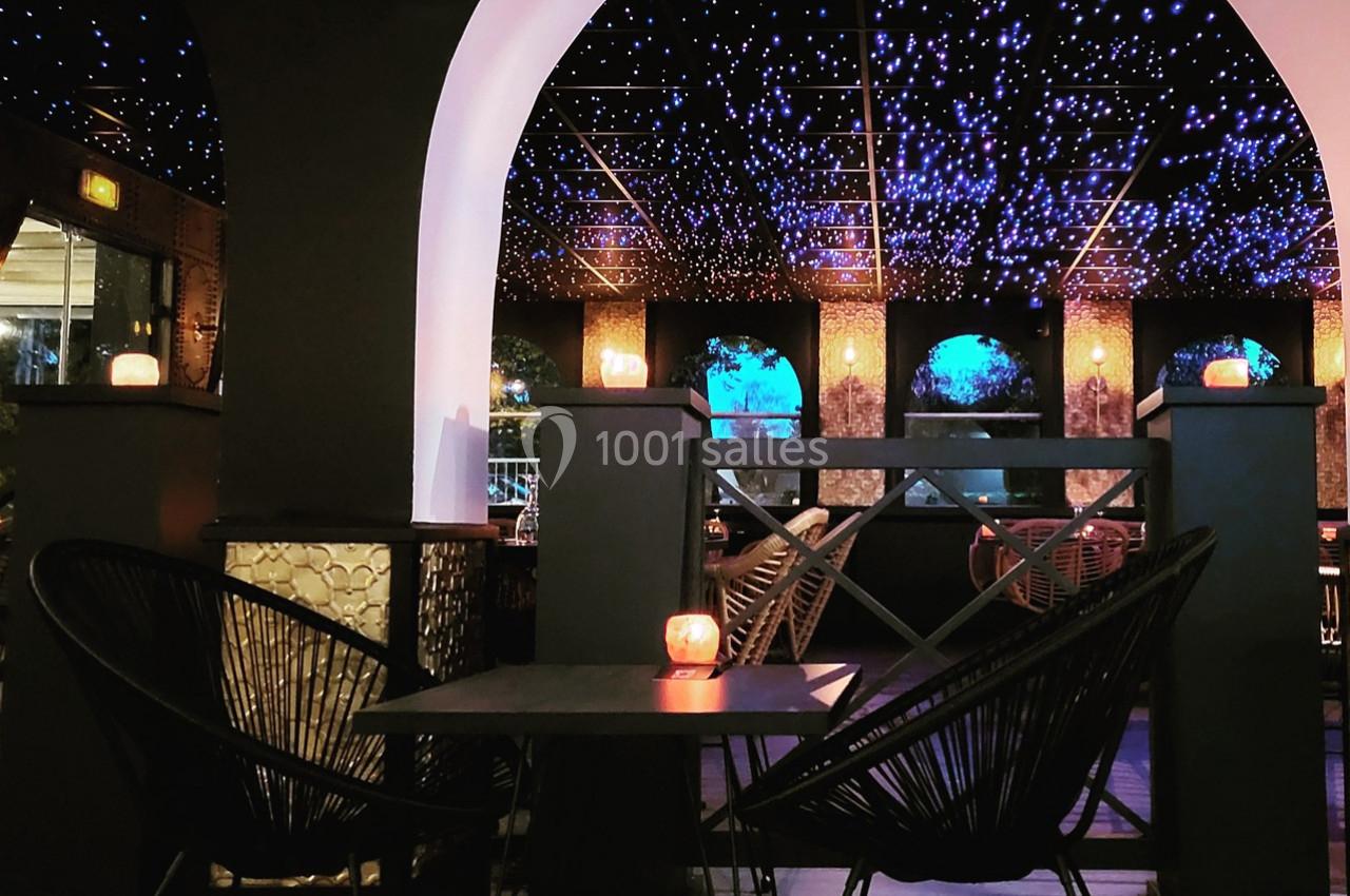 Salle de restaurant avec plafond étoilé, bougies sur les tables et chaises en rotin noir autour d'une table.