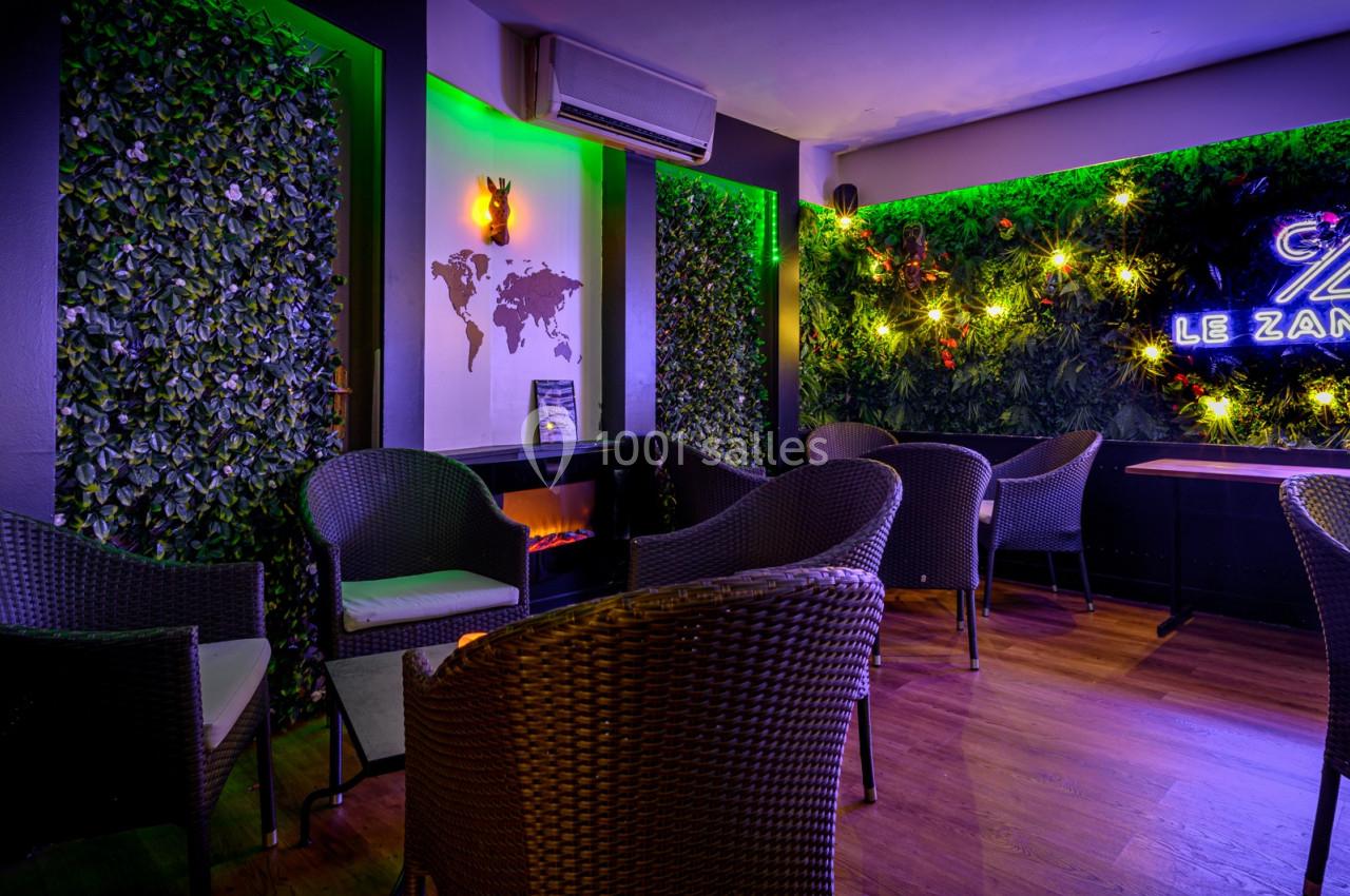 Espace lounge avec fauteuils en rotin, murs végétalisés, éclairage néon et décoration murale moderne.